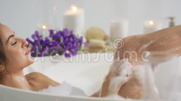 侧面看热女人用泡沫洗腿在家洗澡的浪漫女孩视频的预览图