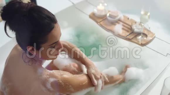 微笑的女人用泡沫洗手性感女孩用蜡烛在浴缸里放松视频的预览图