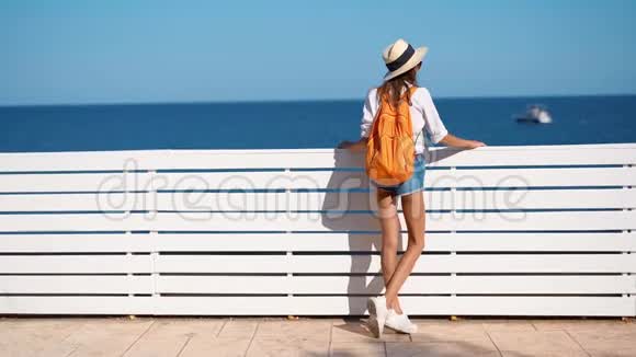 慢动作美女游客穿着太阳帽衬衫和短裤欣赏海景视频的预览图