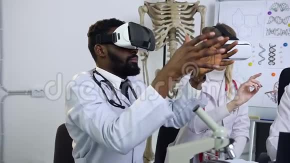 英俊的非裔美国人和美丽的金发医生戴着虚拟现实耳机进行医疗程序视频的预览图
