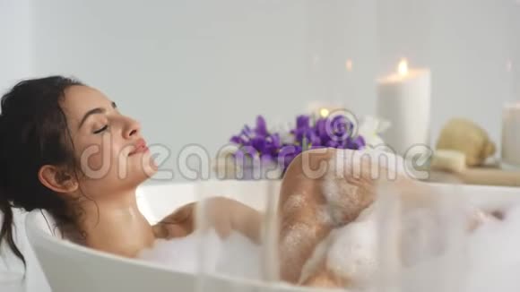 特写放松的女人用泡沫在家里洗澡女人吹着泡沫视频的预览图