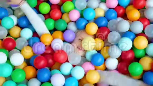 可爱的金发小女孩躺在多种颜色的塑料球在大干划水池在游戏中心微笑着视频的预览图