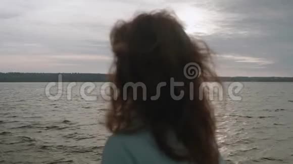 深色头发的后视图长发站立在码头前水天空和水的背景视频的预览图
