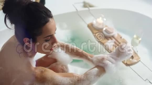 放松的女人用泡沫洗手性感女孩在泡沫浴中摸脖子视频的预览图