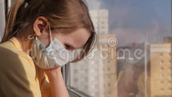 检疫威胁冠状病毒悲伤的孩子戴着防护医疗面具坐在窗台上看着窗外病毒视频的预览图