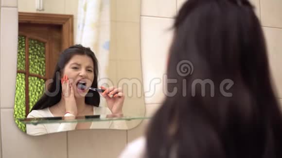 年轻女子刷牙时剧烈的牙痛抚摸她的脸颊视频的预览图