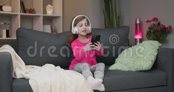 戴着蓝牙耳机的小女孩在智能手机上欣赏着mp3播放器的音乐视频的预览图