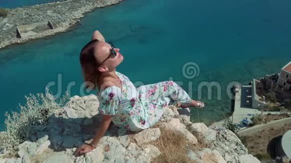 穿裙子的女人坐在海边的悬崖边上视频的预览图