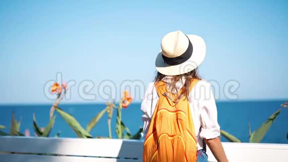 后景慢动作年轻女子旅游草帽和橙色背包享受海景在海边阳光明媚的日子视频的预览图