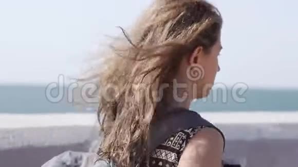 一个女孩带着背包和无线耳机沿着海滨散步视频的预览图