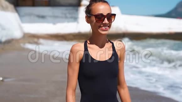慢动作苗条性感健康微笑年轻的女人穿着黑色泳装带着波浪在海边散步视频的预览图
