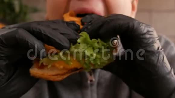 戴着黑色橡胶手套的少年正在吃汉堡美味多汁的新鲜汉堡摆在桌上的快餐视频的预览图
