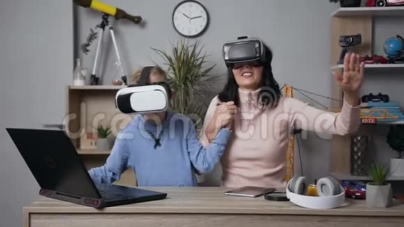 漂亮的黑发年轻女子与她的少女微笑的儿子玩电子游戏使用保护虚拟3D眼镜视频的预览图