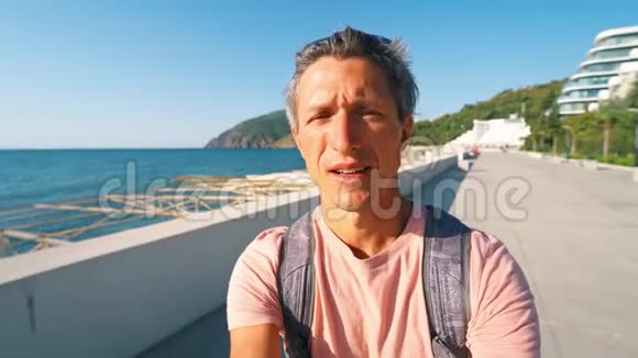 阳光明媚的一天英俊的微笑晒黑了的男子旅行者旅游博主在海滨湾拍摄视频自拍视频的预览图