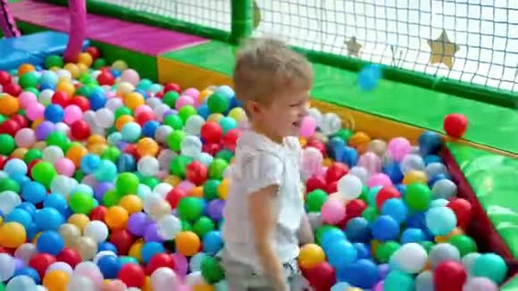 金发的小男孩把球分散在不同的侧面躺在多种颜色的塑料球上在大干划池里视频的预览图