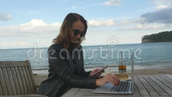 在户外咖啡馆里用笔记本电脑和手机工作的年轻女性视频的预览图