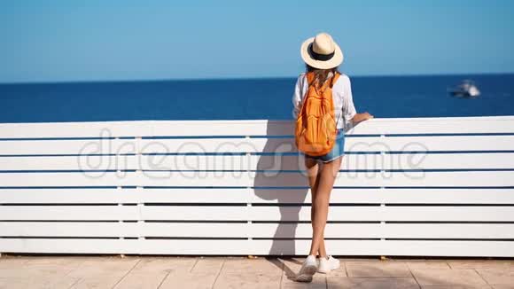 后景女游客戴草帽白色衬衫和橙色背包享受和海景在晴天视频的预览图