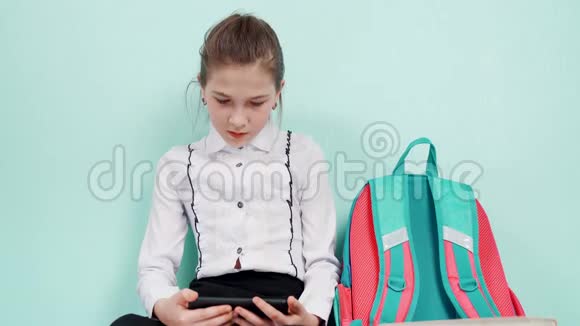 一个穿着蓝色背景白色衬衫的年轻女生坐在地板上手里拿着一部智能手机旁边是一个视频的预览图