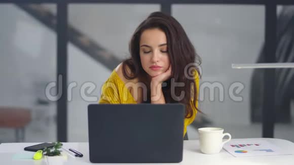 疲惫的女商人在室内伸展手臂工作过度的女孩在笔记本电脑附近打哈欠视频的预览图