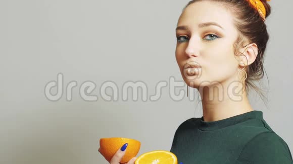 年轻的女人有着明亮的妆容手里拿着一半的橙色摆着姿势脸上挂着快乐的女孩健康的饮食观念时尚视频的预览图