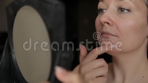 一个女人用镜子检查她脸上的剥落视频的预览图