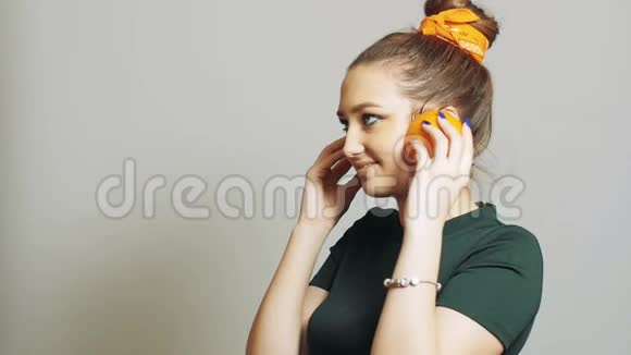 漂亮的女孩把橘子的一半水果放进耳朵里就像耳机一样青少年在演播室背景下玩得很开心概念时尚视频的预览图