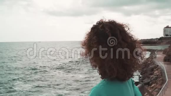 阴天时美丽的卷发黑发女人看着大海视频的预览图