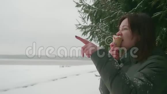 侧面看穿绿色外套的女人在冬天在外面吃冰淇淋用手指指向方向她做到了视频的预览图