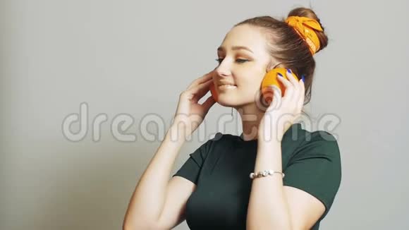漂亮的女孩把橘子的一半水果放进耳朵里就像耳机一样十几岁的孩子在演播室的背景下玩得很开心视频的预览图