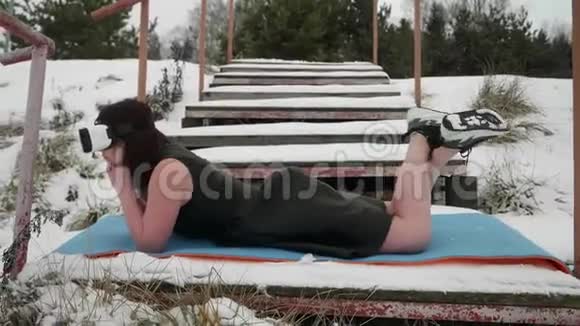 一个穿着巴尔克服装的女孩躺在地上白雪覆盖环顾四周布鲁内特戴着VR眼镜假装视频的预览图