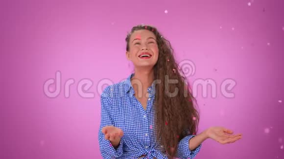 美丽的卷发女孩在孤立的粉红色背景下站在雨中的纸屑视频的预览图