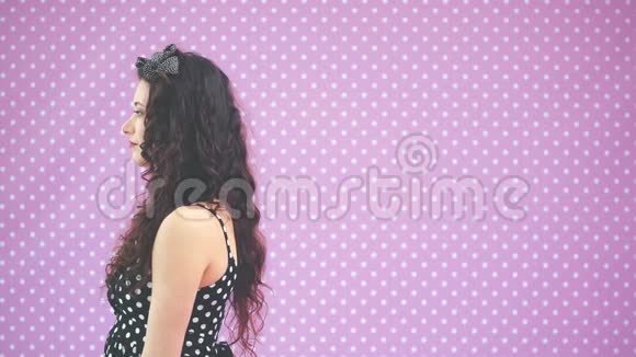 美丽的年轻女孩一头古怪的头发穿着漂亮的黑色圆点花裙站在侧面然后转过身来看着视频的预览图