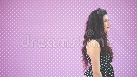 美丽的年轻女孩一头古怪的头发穿着漂亮的黑色圆点花裙站在侧面然后转过身来看着视频的预览图