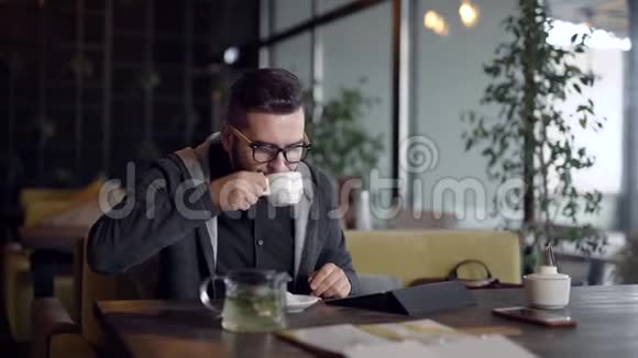 独自一人的年轻人白天独自在咖啡馆里休息用平板电脑喝着杯子里的热茶视频的预览图
