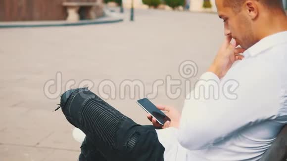一直保持联系年轻人在外面使用智能手机而坐在长凳上作物后景快关门副本视频的预览图