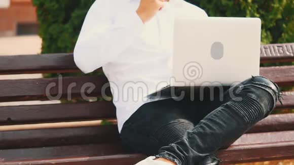 一个面目全非的男人穿着商业风格坐在户外的时候在笔记本电脑上打字视频的预览图
