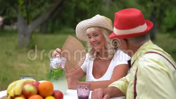 在风景如画的花园里坐在桌子旁的一对老夫妇互相看着对方的眼睛视频的预览图