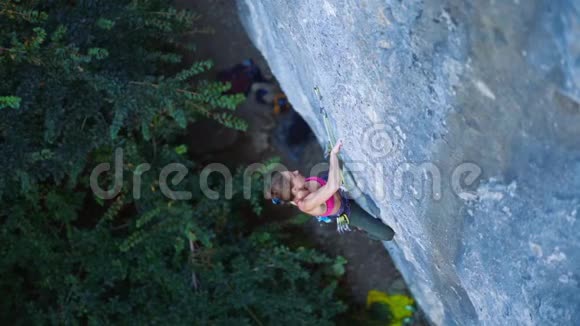 俯视女子攀岩者在艰难的运动路线上攀爬攀岩者休息粉笔手挂在悬崖上视频的预览图
