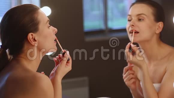 年轻的黑发女人涂着口红看着镜子视频的预览图