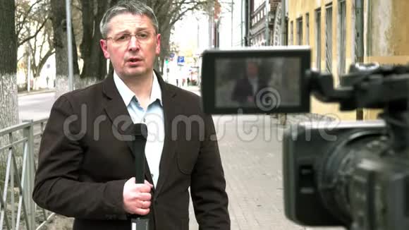 一位中年欧洲记者正在一条城市街道上报道视频的预览图