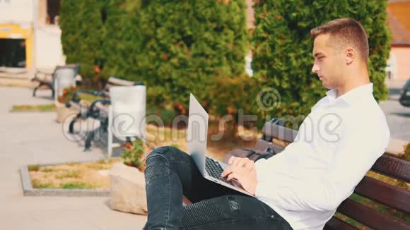 专心致志的男人穿着商业风格坐在公园里的户外在笔记本电脑上打字视频的预览图