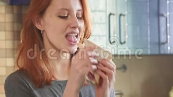 迷人的年轻红发女孩在周末在厨房里吃一个俱乐部三明治女人不健康视频的预览图