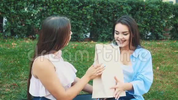 两个漂亮的女孩坐在公园的长凳上金发女孩给她的黑发女人买了一件新的脱光上衣视频的预览图