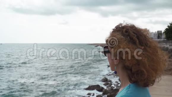 阴天时美丽的卷发黑发女人看着大海视频的预览图
