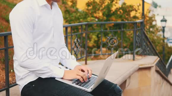 无法辨认的男人穿着商业风格坐在公园外面的时候在笔记本电脑上打字视频的预览图