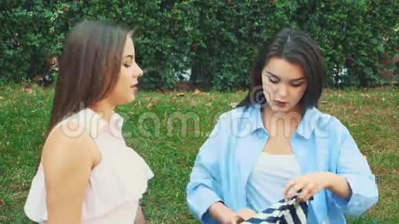 两个漂亮的女孩坐在公园的长凳上布鲁内特买了一件新的脱光上衣但她的衬衫不视频的预览图