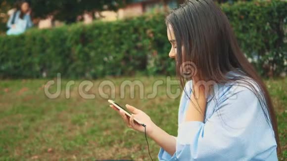 漂亮可爱的女孩在公园里用耳机听音乐快关门侧视复制空间4K视频的预览图