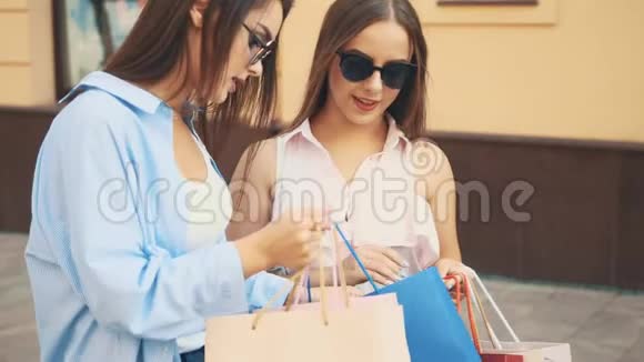 两个有魅力的年轻女人正在谈论购物他们互相展示购买快关门复制空间4K视频的预览图