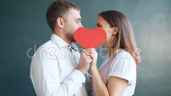 年轻漂亮的情侣在灰色背景的情人节贺卡后面接吻视频的预览图