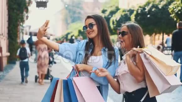 微笑的十几岁女孩正在通过智能手机自拍正在夏季城市公园的背景他们正在购物视频的预览图